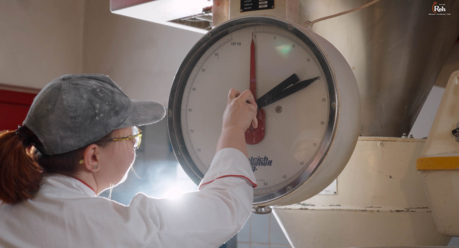 Eine Frau bedient eine Waage. Hier wird Mehl aus einem Silo befördert. Die Frau trägt eine Cap. 4kFactory hat hier ein Video erstellt.