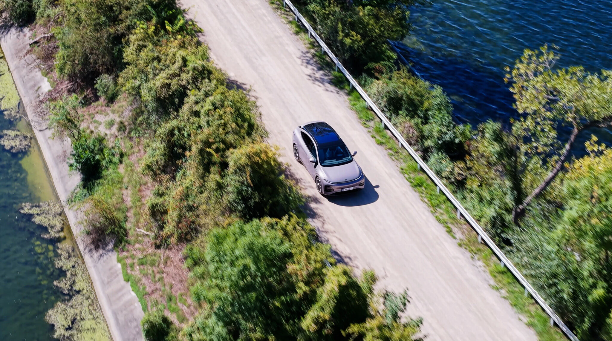 "Luftaufnahme (Top-Down) eines XPENG G6 auf einer Uferstraße neben einem See, produziert während eines Automotive-Videodrehs.“