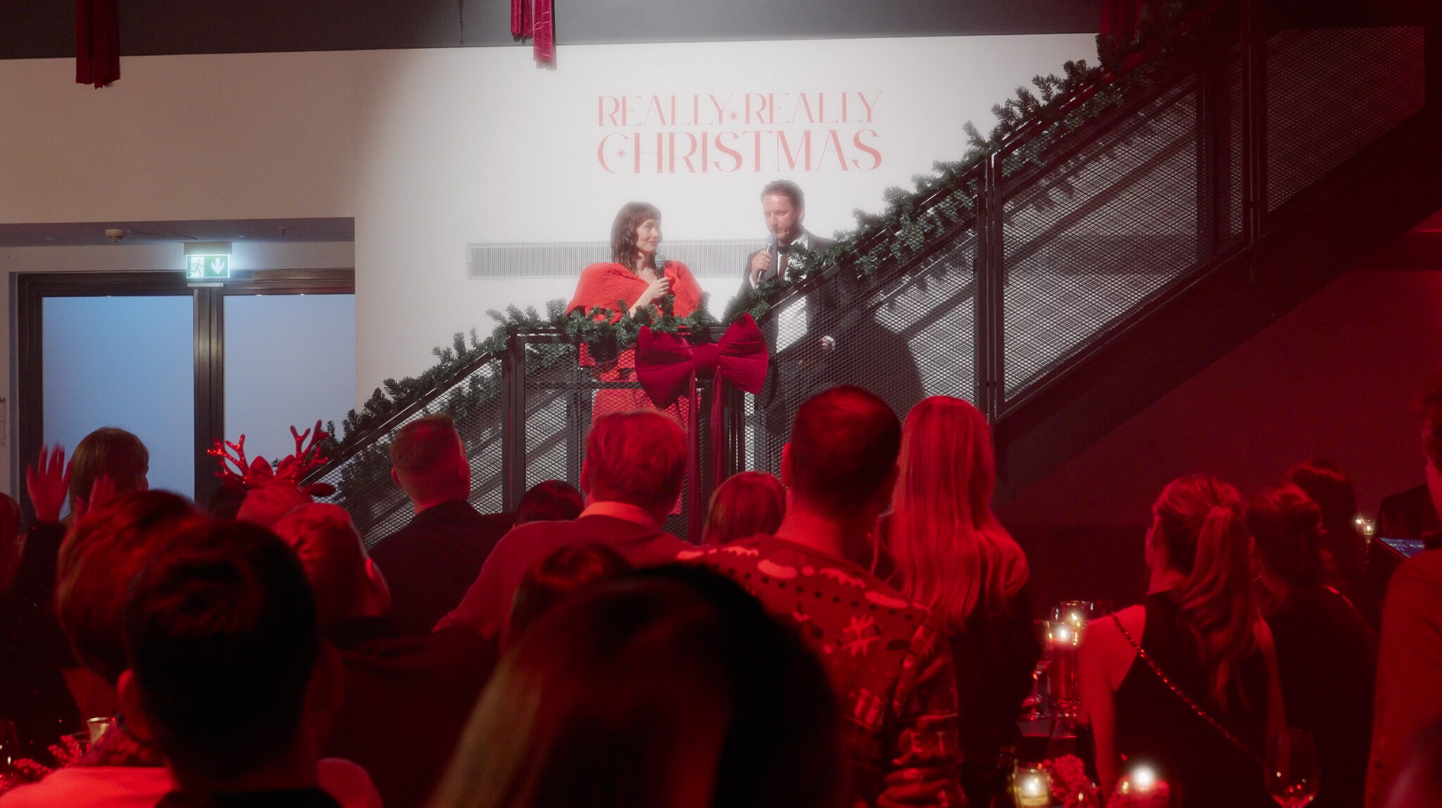 Rede der neuen CEOs auf der Weihnachtsfeier von Avantgarde: Zwei Personen sprechen mit Mikrofonen auf einer festlich dekorierten Treppe vor dem Schriftzug „REALLY REALLY CHRISTMAS“, gefilmt von 4kFactory in München.