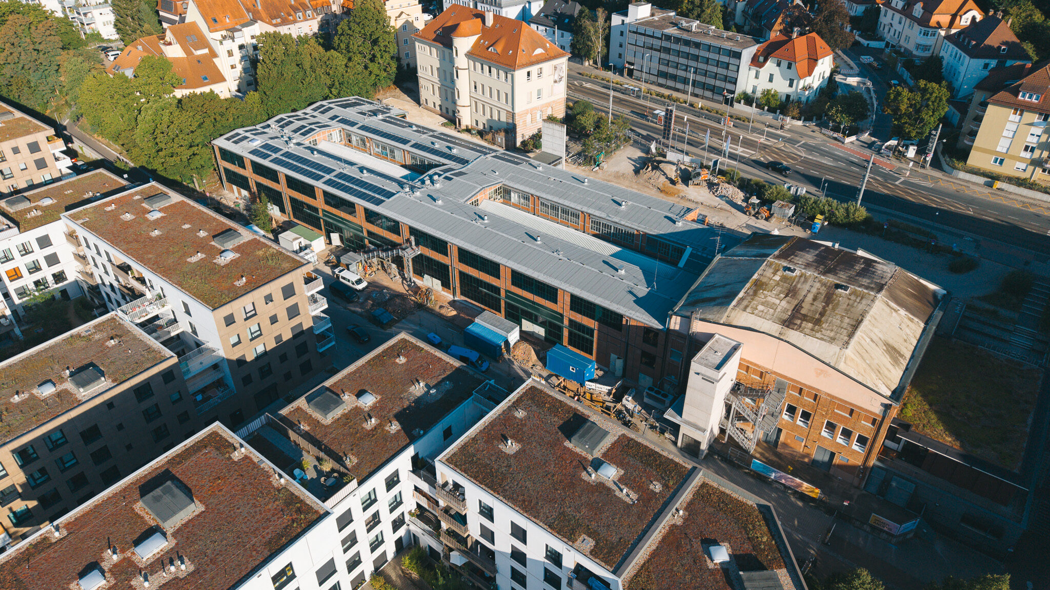 alt="Drohnenaufnahme des Drehortes von 4kFactory in Nürnberg nahe dem Schulmuseum. Die Luftansicht zeigt den modernen Gebäudekomplex mit Photovoltaikanlagen inmitten eines urbanen Wohngebiets."