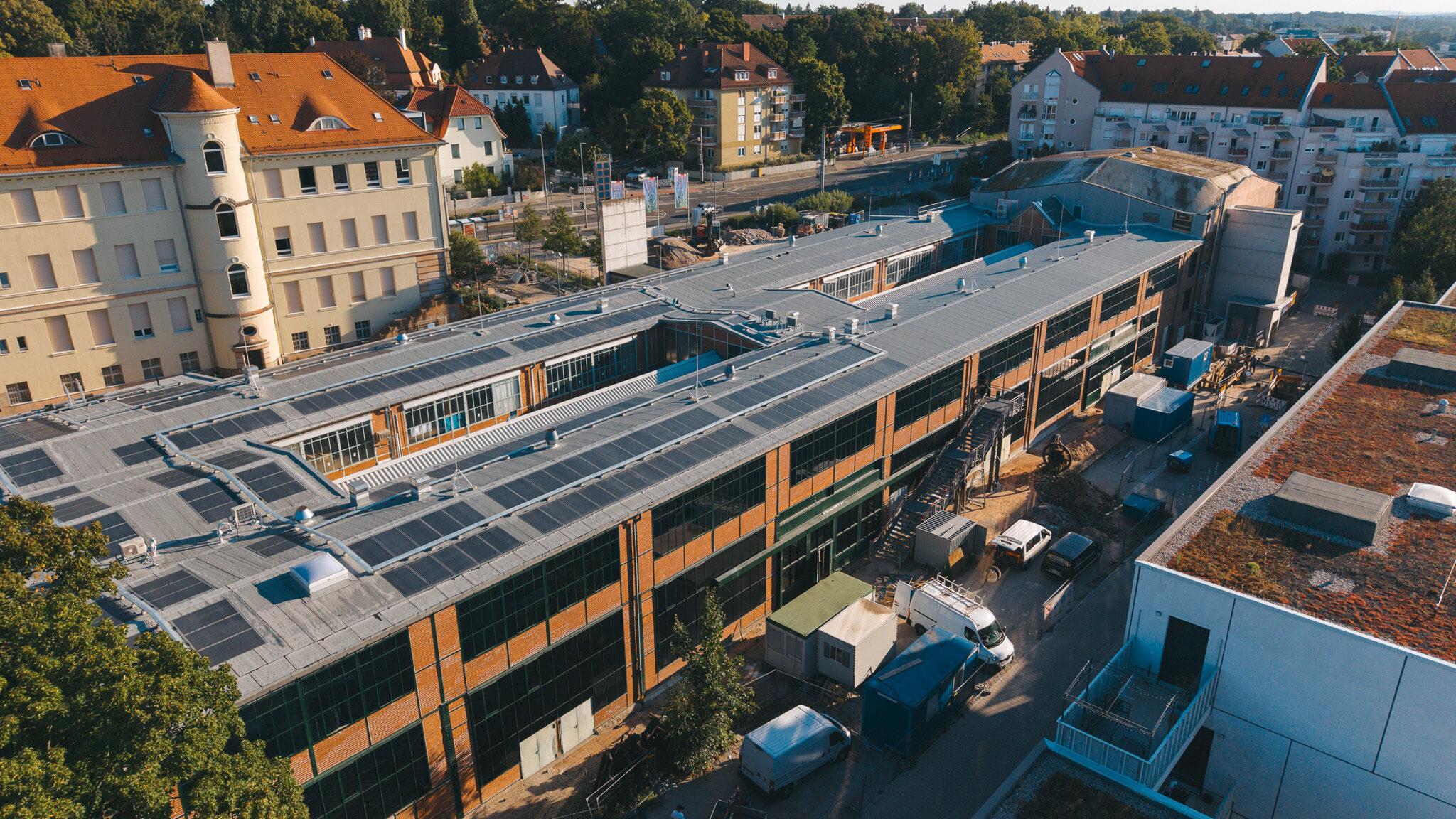 alt="Drohnenaufnahme des Drehortes von 4kFactory in Nürnberg nahe dem Schulmuseum. Die Luftansicht zeigt den modernen Gebäudekomplex mit Photovoltaikanlagen inmitten eines urbanen Wohngebiets."