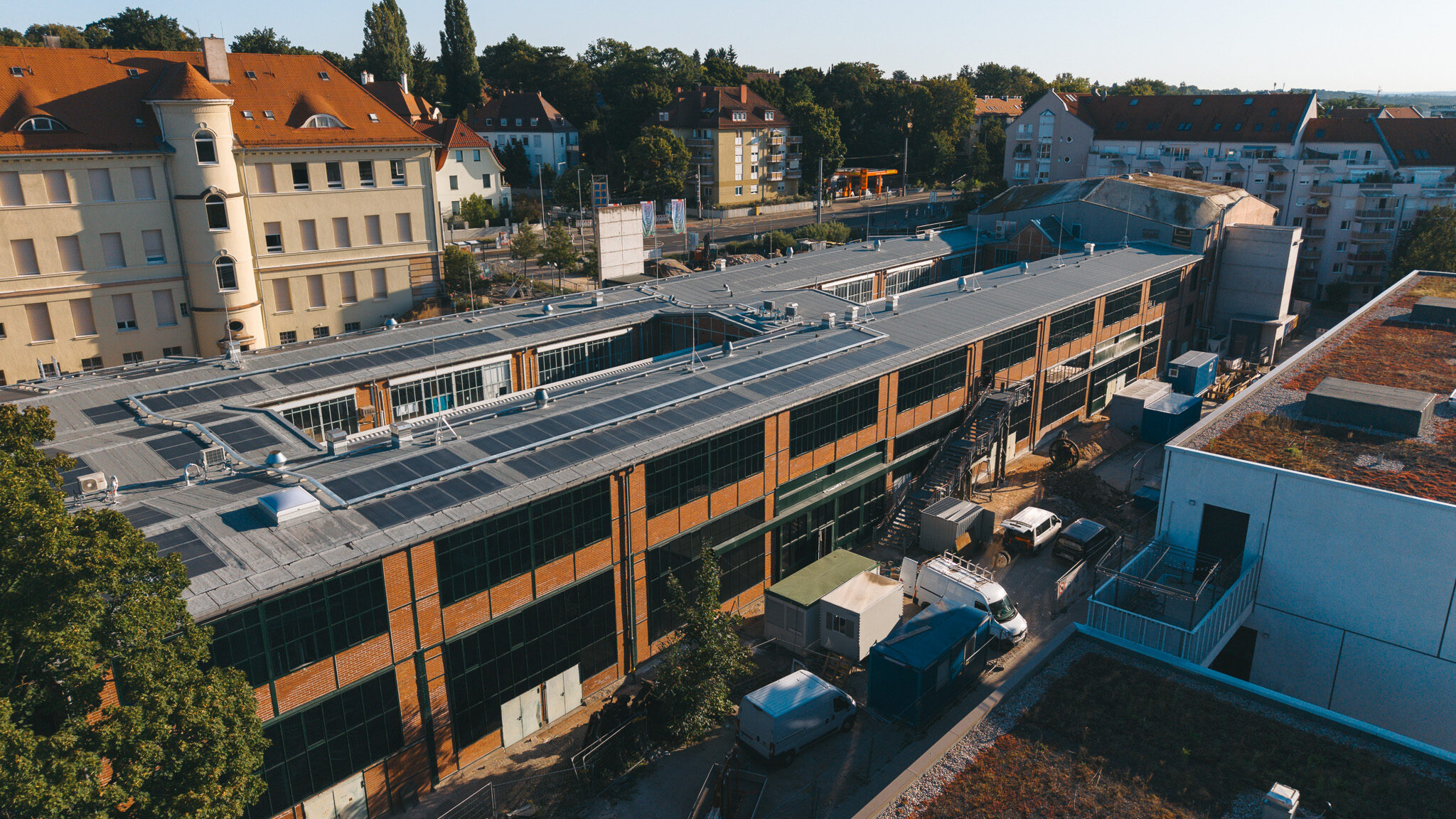 alt="Drohnenaufnahme des Drehortes von 4kFactory in Nürnberg nahe dem Schulmuseum. Die Luftansicht zeigt den modernen Gebäudekomplex mit Photovoltaikanlagen inmitten eines urbanen Wohngebiets."