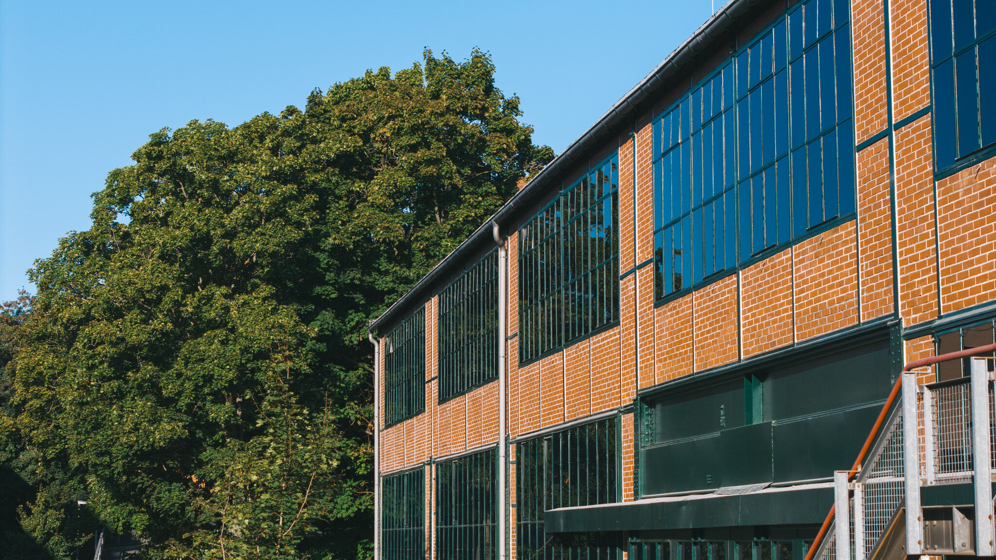 alt="Außenansicht einer industriellen Dreh-Location der 4kFactory in Nürnberg. Das Backsteingebäude mit großen Fensterfronten dient als authentische Kulisse für moderne Content-Produktionen."