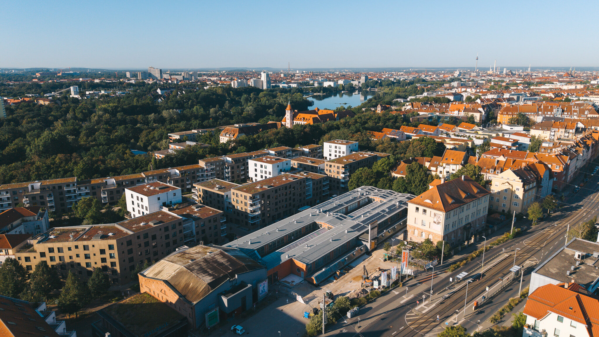 alt="Drohnenaufnahme des Drehortes von 4kFactory in Nürnberg nahe dem Schulmuseum. Die Luftansicht zeigt den modernen Gebäudekomplex mit Photovoltaikanlagen inmitten eines urbanen Wohngebiets."