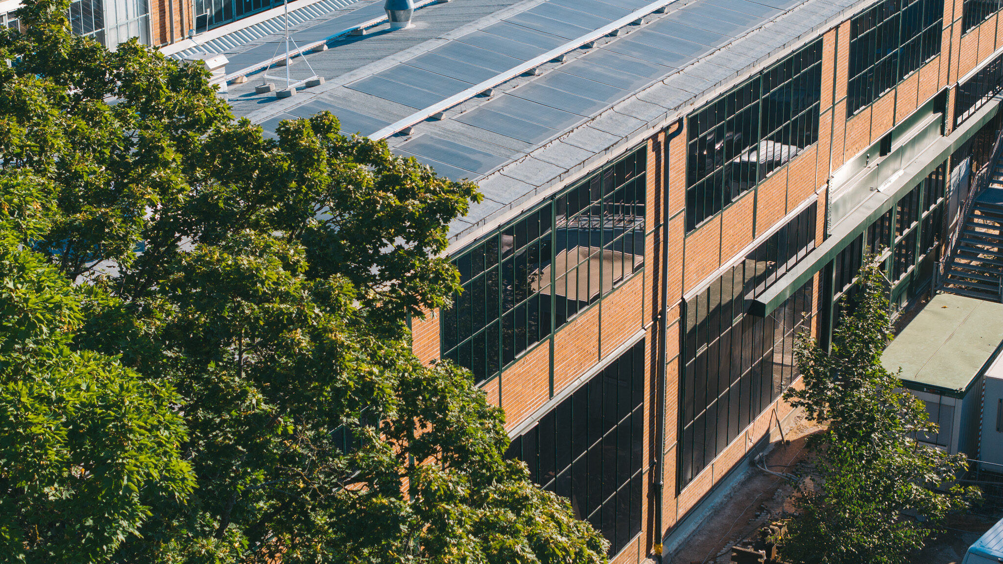 alt="Drohnenaufnahme des Drehortes von 4kFactory in Nürnberg nahe dem Schulmuseum. Die Luftansicht zeigt den modernen Gebäudekomplex mit Photovoltaikanlagen inmitten eines urbanen Wohngebiets."