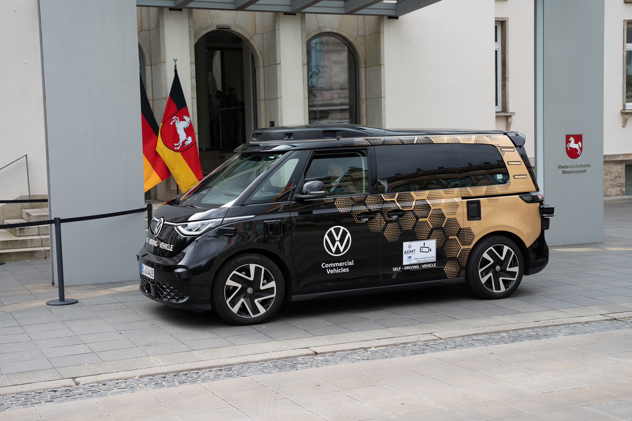 Repräsentative Corporate-Produktion von 4kFactory: Das autonome MOIA-Testfahrzeug vor der Niedersächsischen Staatskanzlei in Hannover, flankiert von der Landesflagge und dem offiziellen Landeswappen. Es ist Tag und bewölkt.