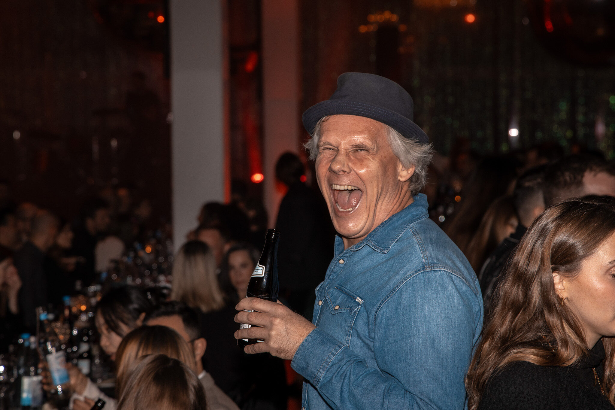 4kFactory Corporate Event Dokumentation: Festlich gedeckter Gala-Saal mit atmosphärischer Beleuchtung und Marken-Branding in München. Mit Mann der lachend in die Kamera schaut.