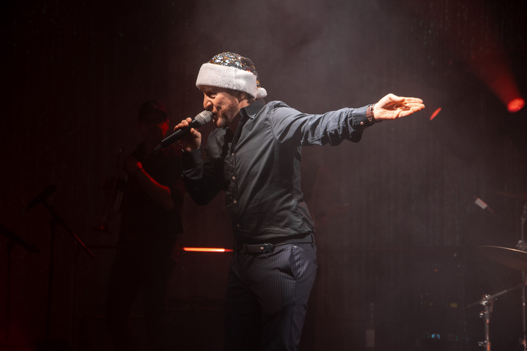 Professionelle Konzertfotografie von 4kFactory: Ein Sänger mit Weihnachtsmütze performt live auf der Bühne während der Avantgarde Weihnachtsfeier in München.