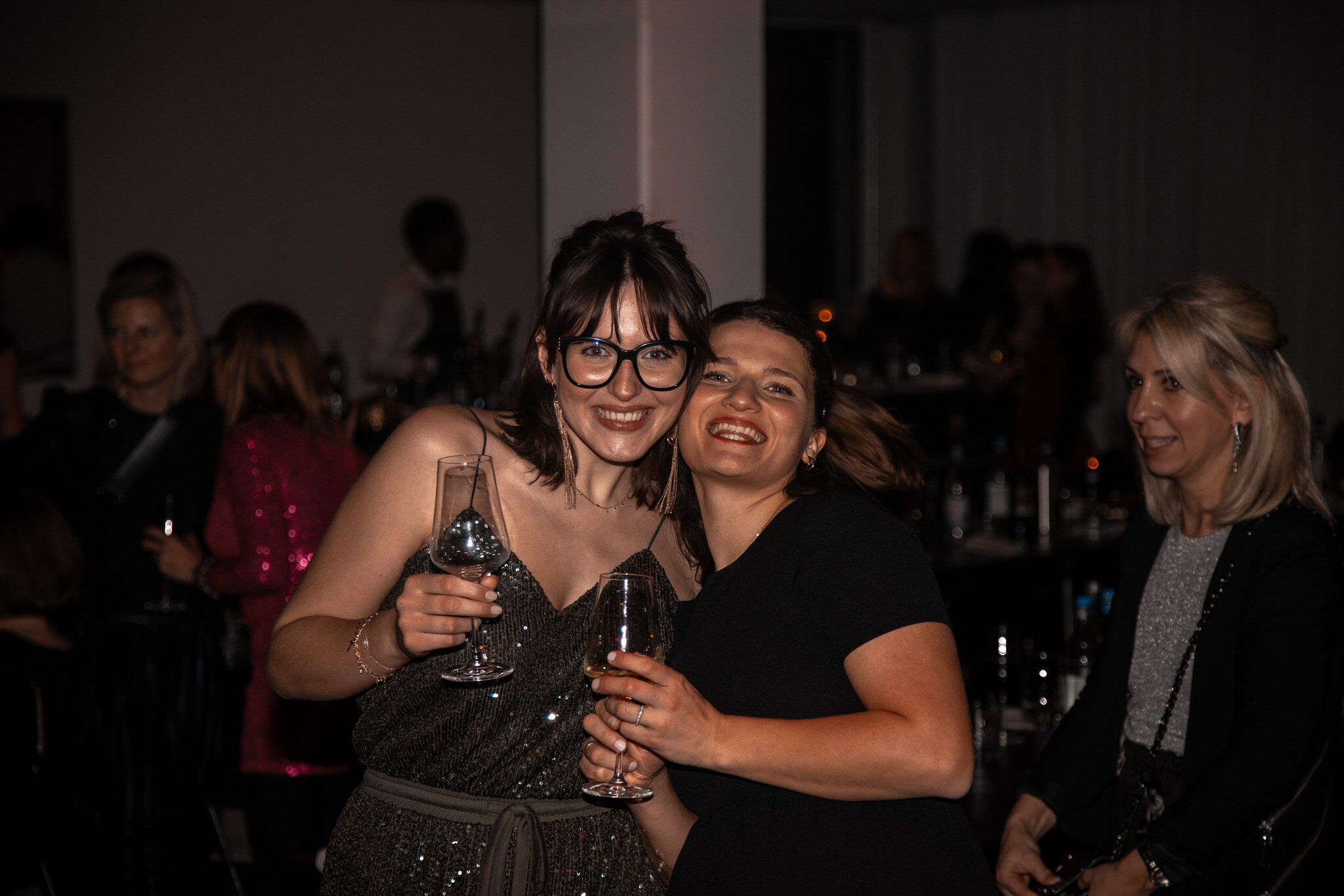Authentische Gäste-Fotografie: 4kFactory fängt zwei lachende Kolleginnen mit Weingläsern ein, die den Teamgeist auf der Firmenfeier von Avantgarde verkörpern.