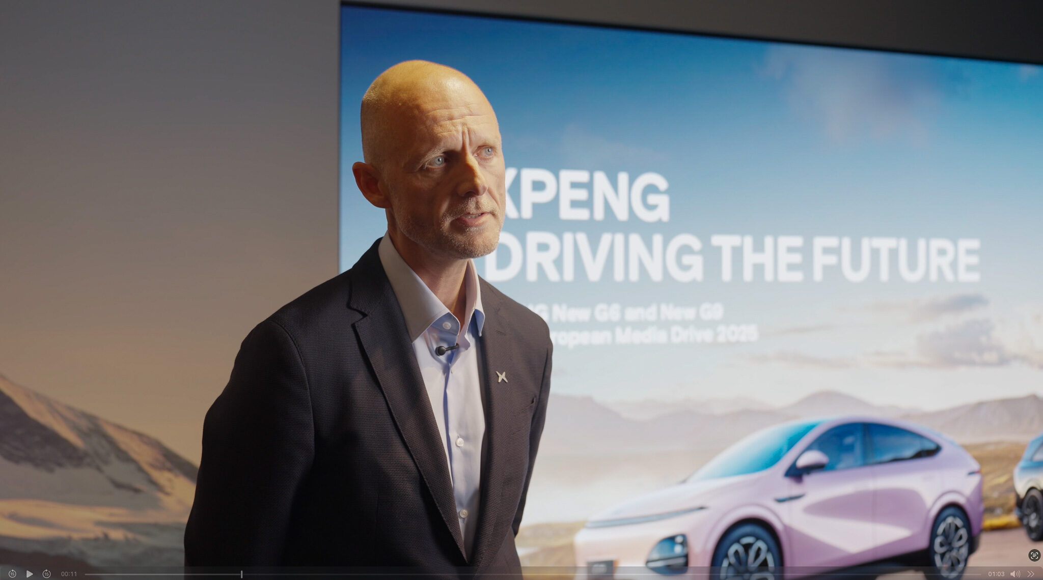 „Ein Mann in dunklem Sakko spricht während einer Automotive-Videoproduktion für XPENG vor einer Leinwand mit der Aufschrift ‚Driving the Future‘ und einem abgebildeten XPENG G6.“
