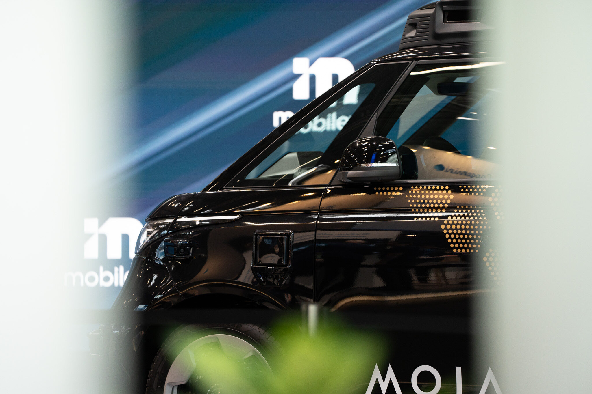 Automotiv Social Media Content von 4kFactory: Die fließenden Formen und integrierte Sensortechnik des autonomen VW ID. Buzz AD am Mobileye-Stand der IAA MOBILITY, kunstvoll durch Unschärfe im Vordergrund gerahmt.